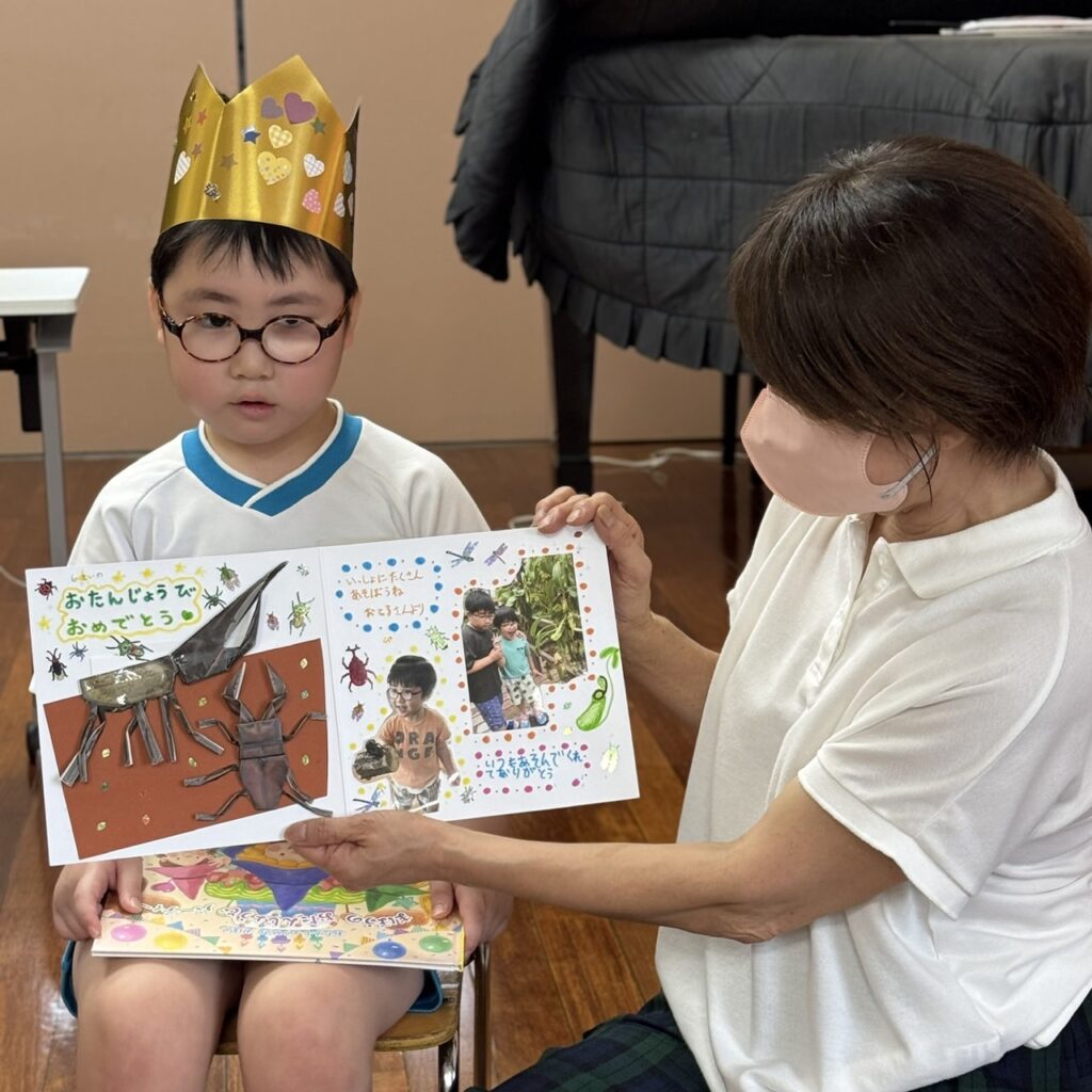 写真やメッセージが入った誕生日カードを先生と見る園児